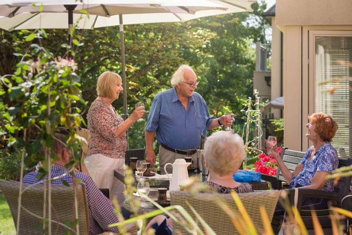 People are enjoying the outdoor seating available on a patio, which is protected from the sun by umbrellas and trees provided by Anchor.