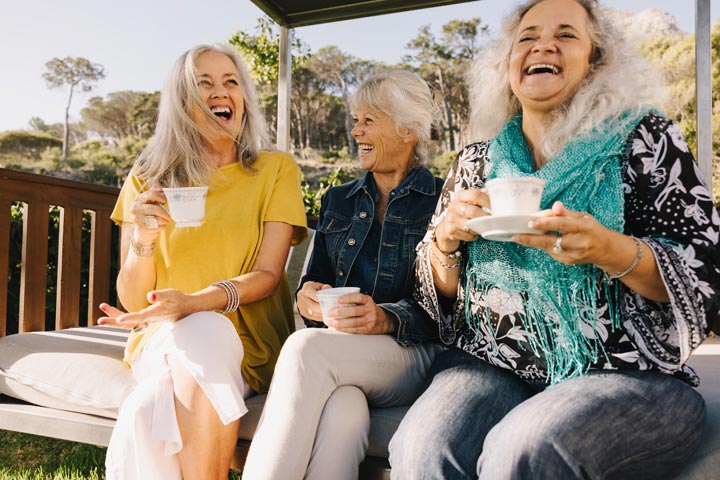 Three residents at Anchor sitting on a bench in the garden, sharing a joyful moment as they laugh together.