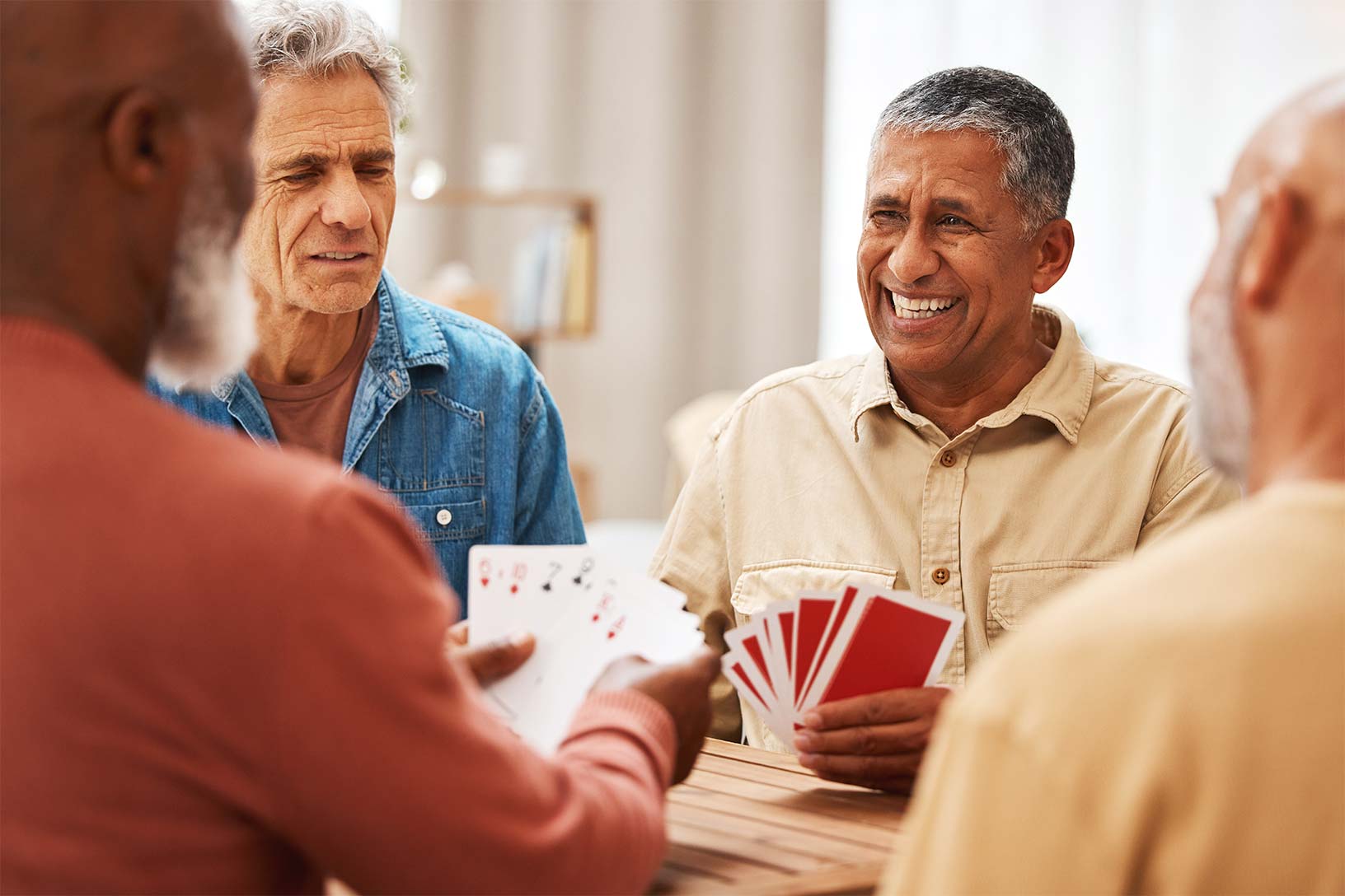 Four friends sitting around a table, engrossed in a game of cards, enjoying their leisure time together in the comfort of their spacious living room.